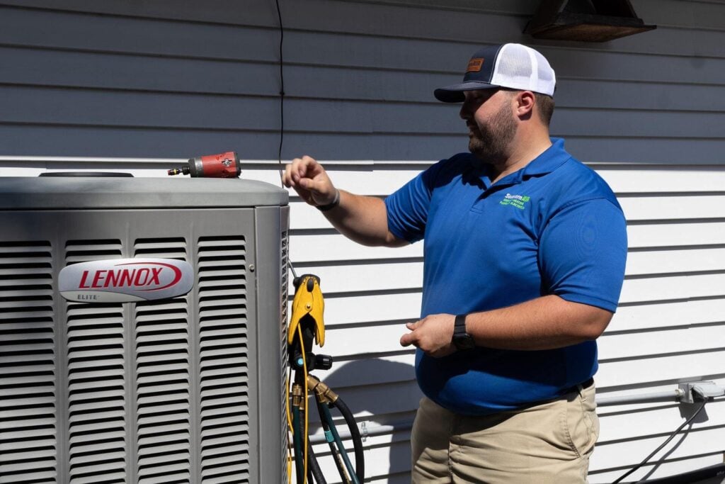 Southern Air technician in blue polo shirt services a Lennox Elite air conditioning unit mounted on exterior wall.