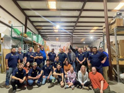 Large group of Southern Air employees wearing navy blue uniforms posing together in a warehouse with a Happy Fall banner.